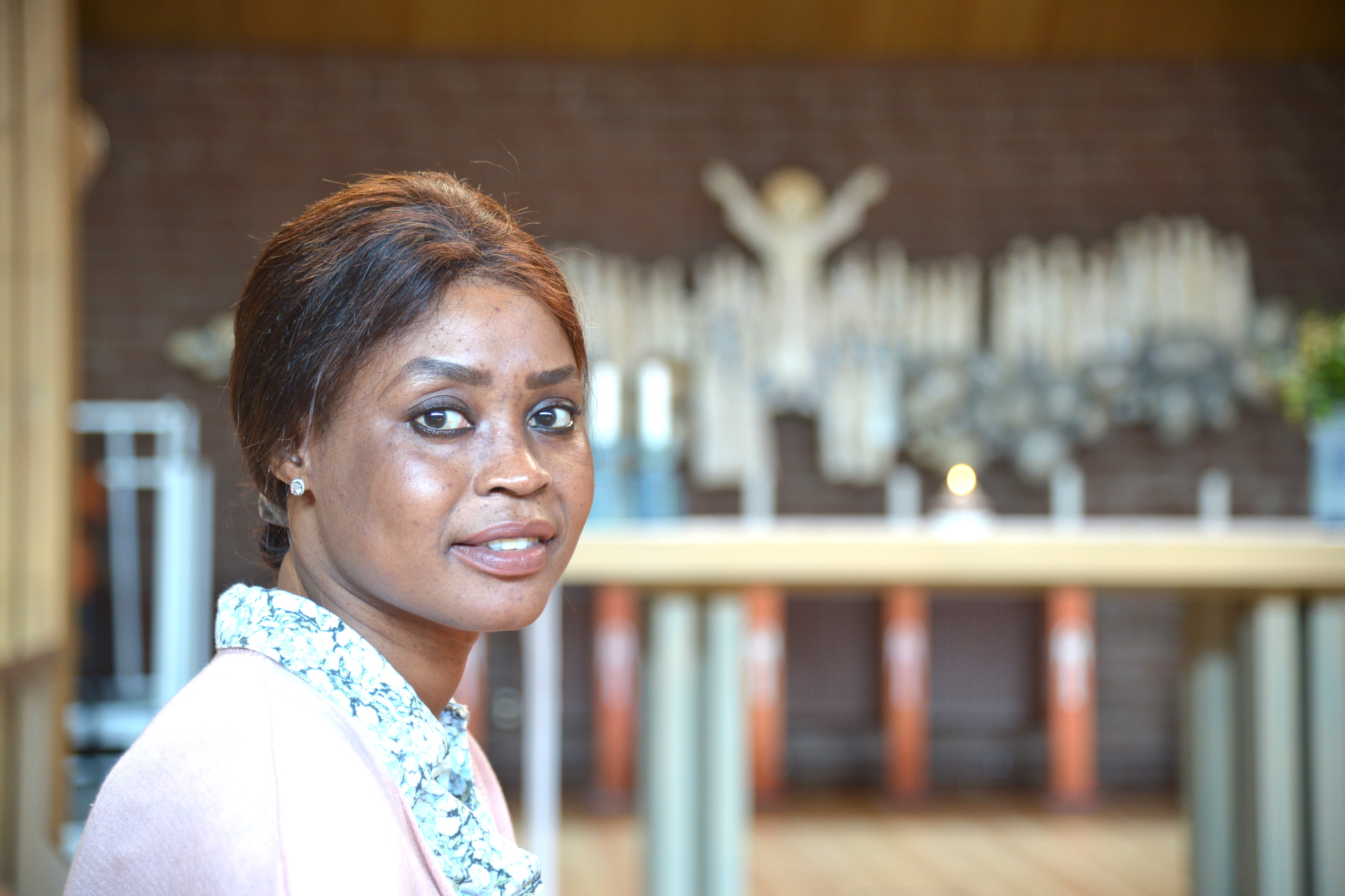 En mörkhyad kvinna sitter på en stol i ett kyrkorum