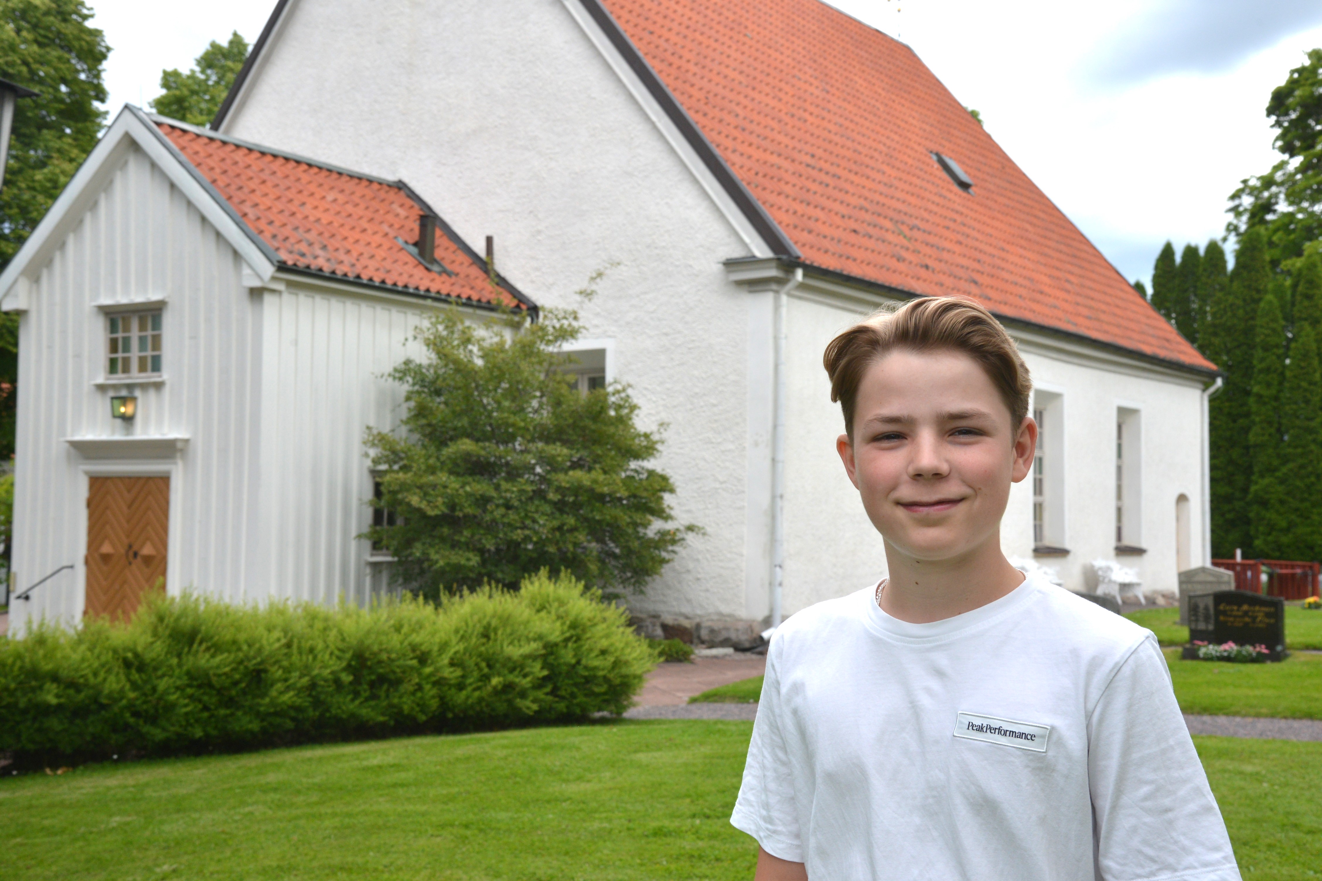 En pojke i vit t-shirt står framför en vit kyrka