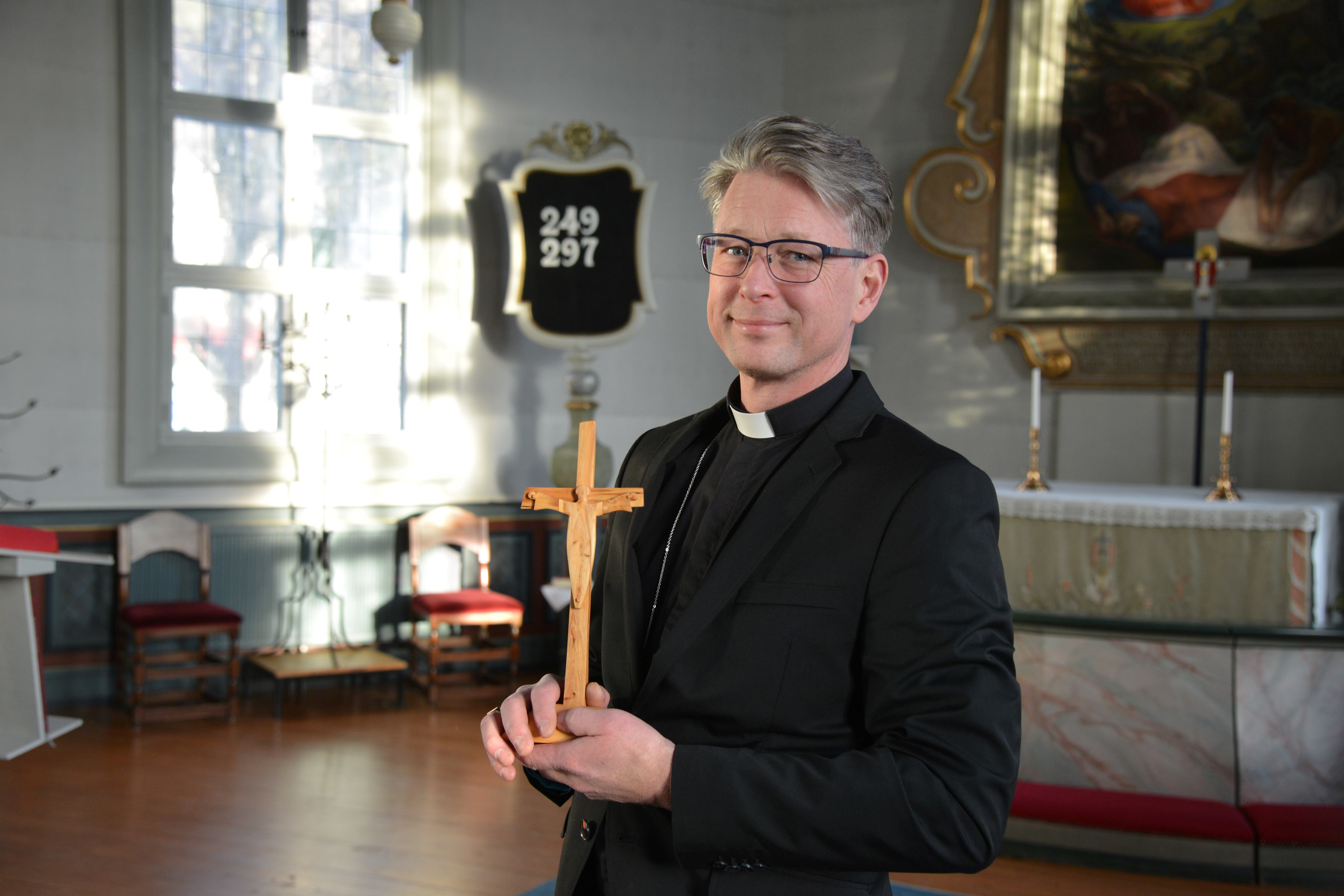en manlig präst står i en kyrka med ett krucifix i handen