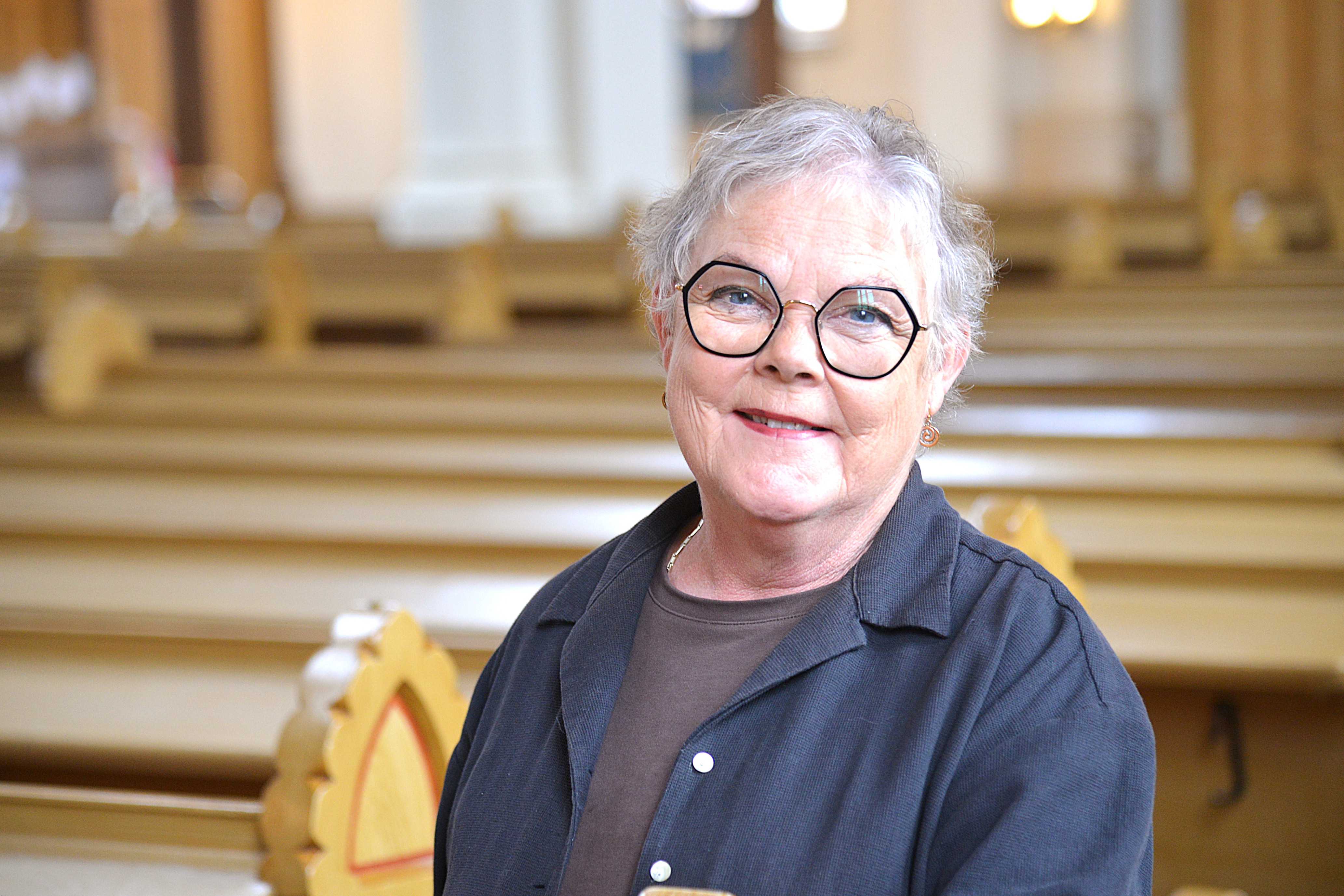 En kvinna står bland bänkarna i en kyrka