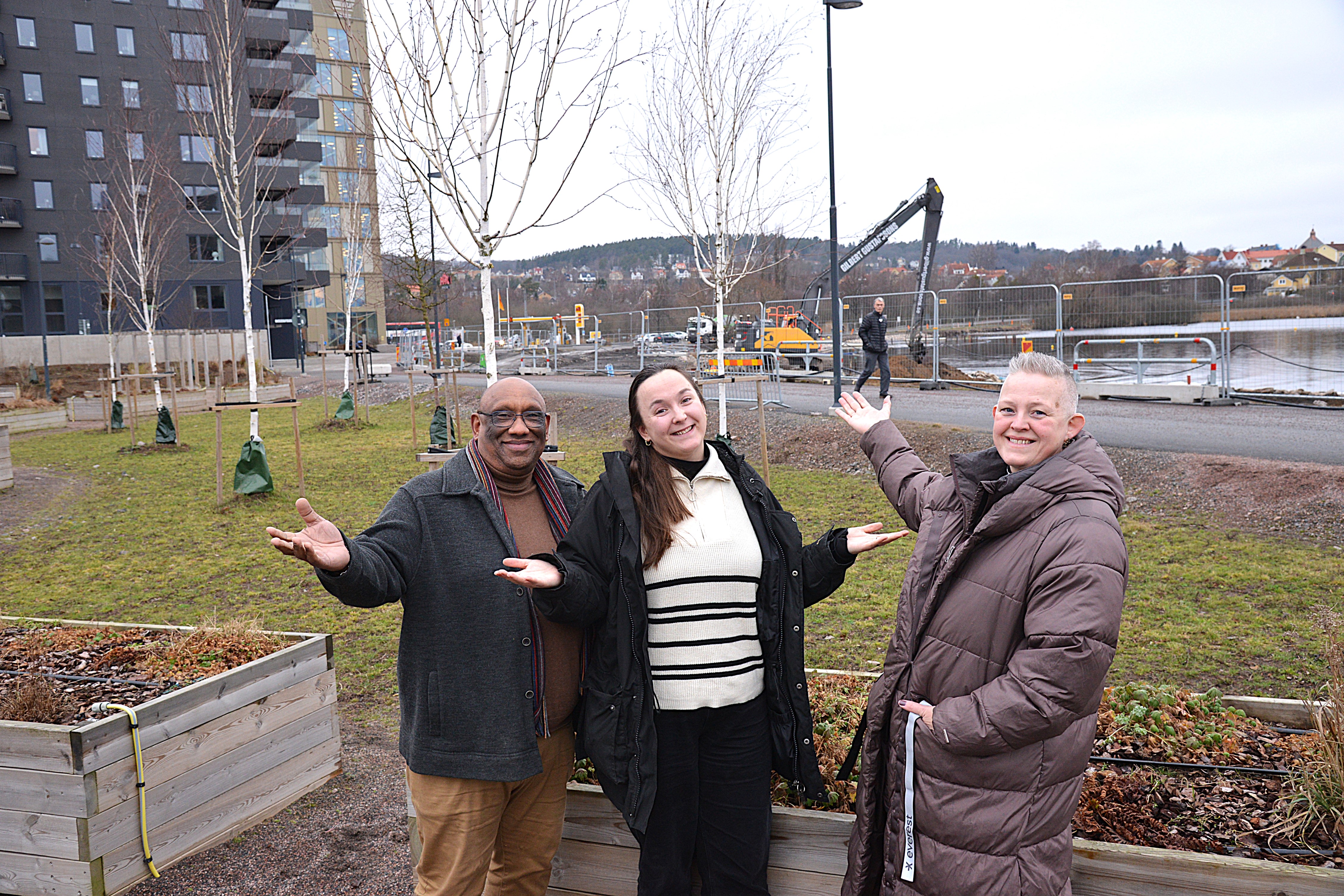 En man och två kvinnor står och slår ut med armarna i ett nytt bostadsområde