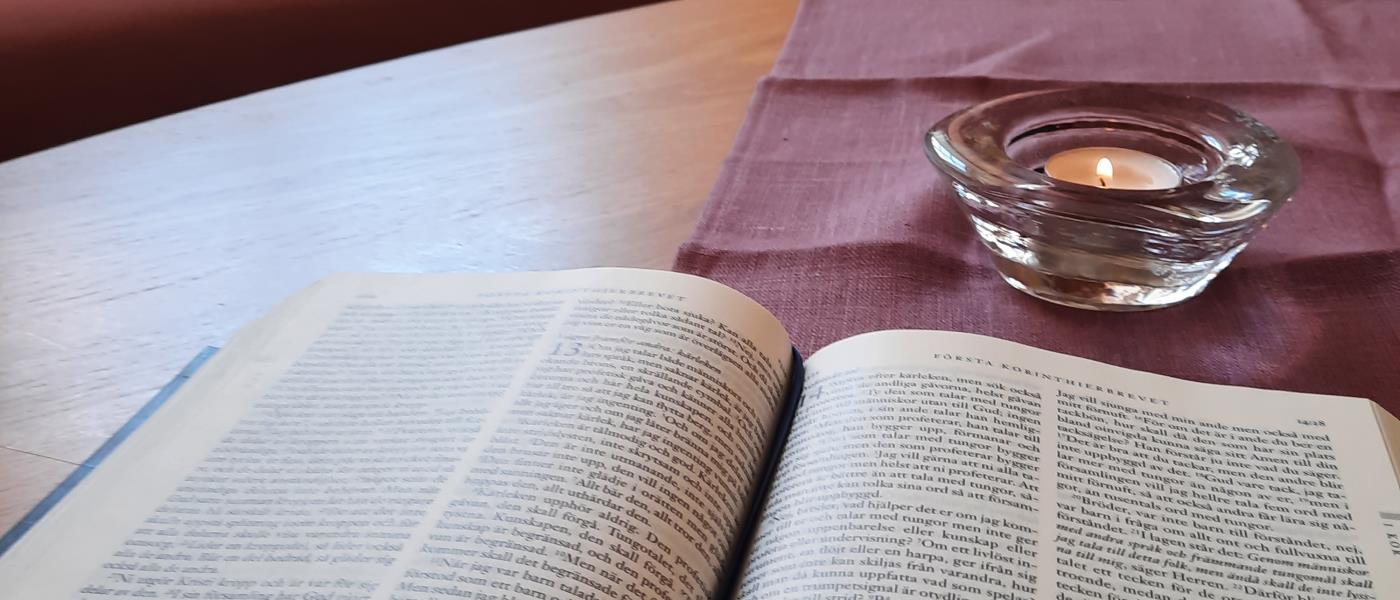 En bild på en uppslagen bibel på ett bord och ett ljus.