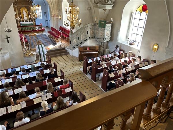 Konfirmander sitter i bänkar i kyrkan