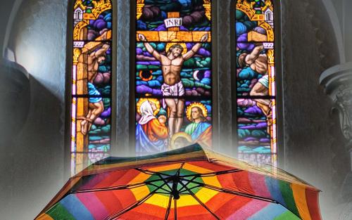 Ett regnbågsfärgat paraply framför ett krucifix i en kyrka.
