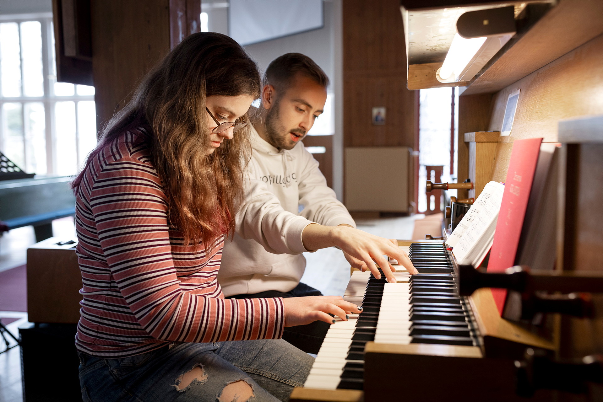 En orgellärare och en elev spelar tillsammans på en orgel.