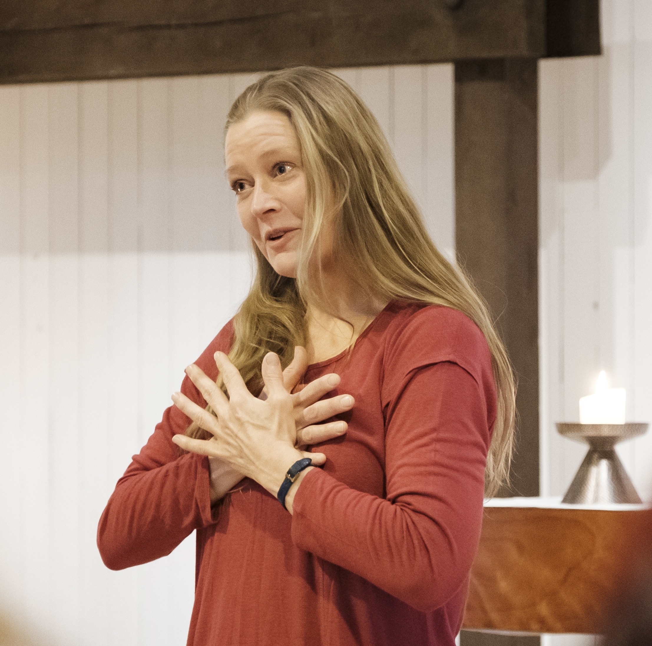Åsa, en blond kvinna med orange tröja håller sin händer korsade över bröstkorgen.