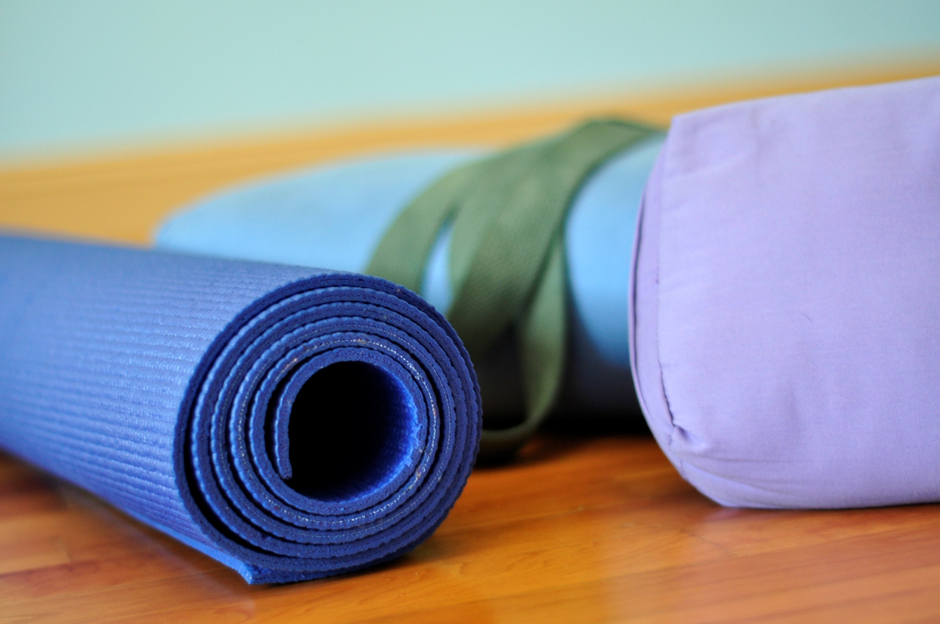 Två kuddar och en hoprullad yogamatta ligger på ett trägolv.