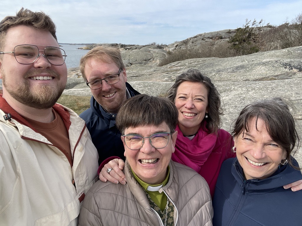 Ett gäng glada medarbetare från kyrkan står på klipporna vid havet.