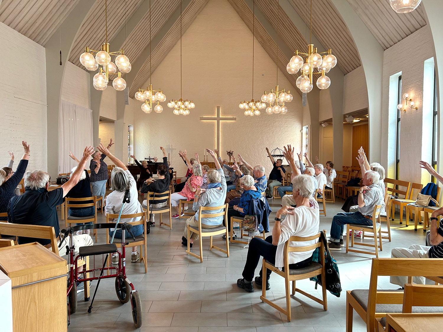 Sittgympa i Näsets kyrksal. Person sitter på stolar i en halvcirkel och sträcker på armarna. 