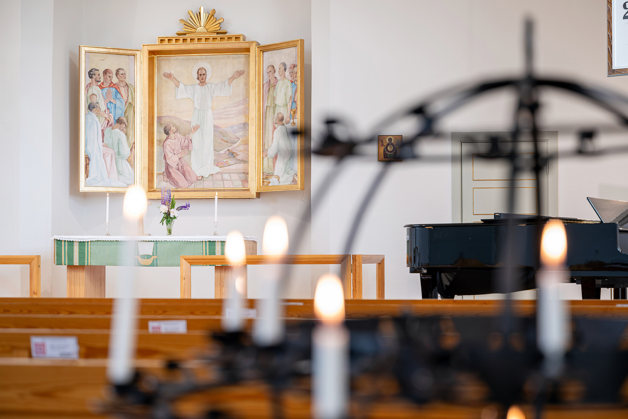 Stämningsfull interiör från Älvsborgs kyrka i varmt ljus, sedd över kyrkbänkar med levande ljus i förgrunden och altartavlan samt en flygel i bakgrunden.