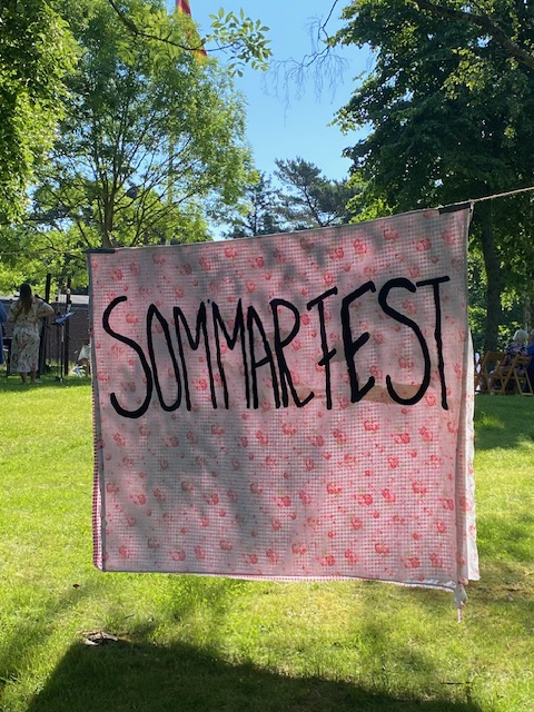 Ett hängande lakan i sommarljus med texten Sommarfest målat på sig.