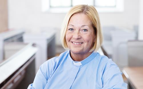 En kvinna med ljust hår och blå skjorta med prästkrage.