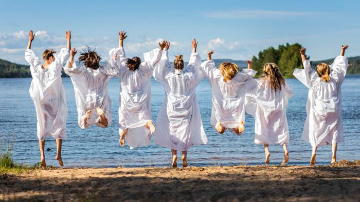 Konfirmationsklädda hoppande ungdomar på en strand