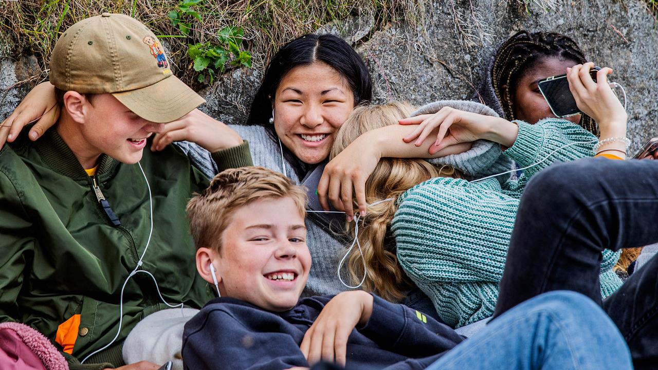 Unga personer sitter lutande mot en stenmur och skrattar.