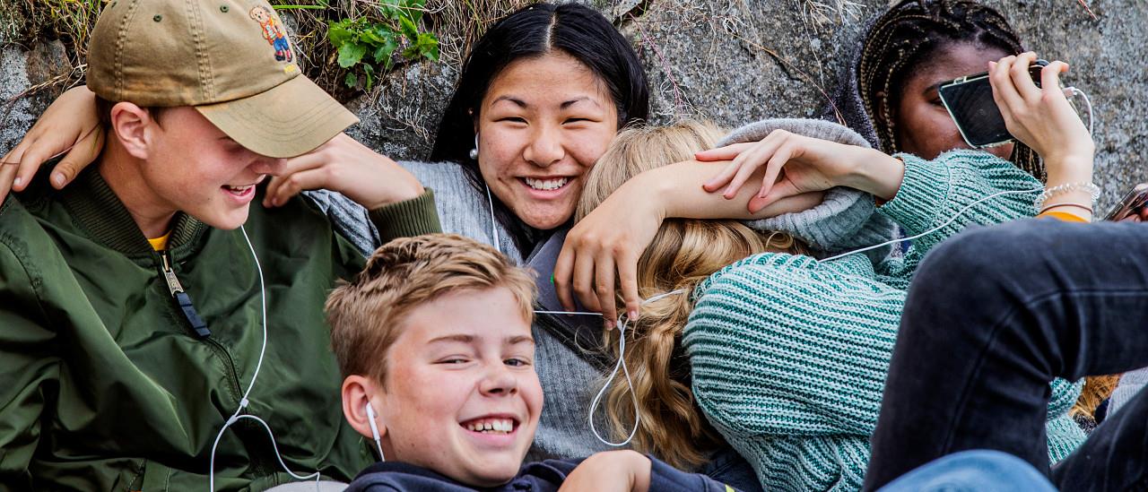 Unga personer sitter lutande mot en stenmur och skrattar.