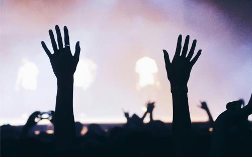 Två händer sträcker sig i luften i en publik, i bakgrunden konsertljus.