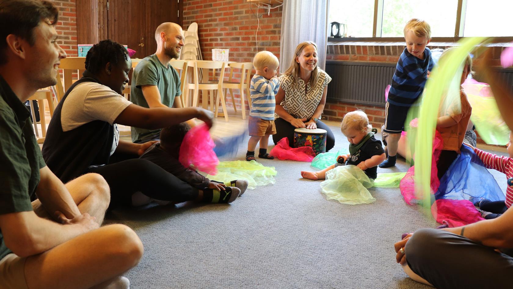 Föräldrar och barn sitter i en ring och viftar med sjalar i olika färger.