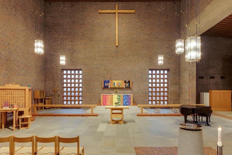 Koret med altaret i mitten omgärdat av två stora fönster och ett t-format kors längst uppe vid taket.