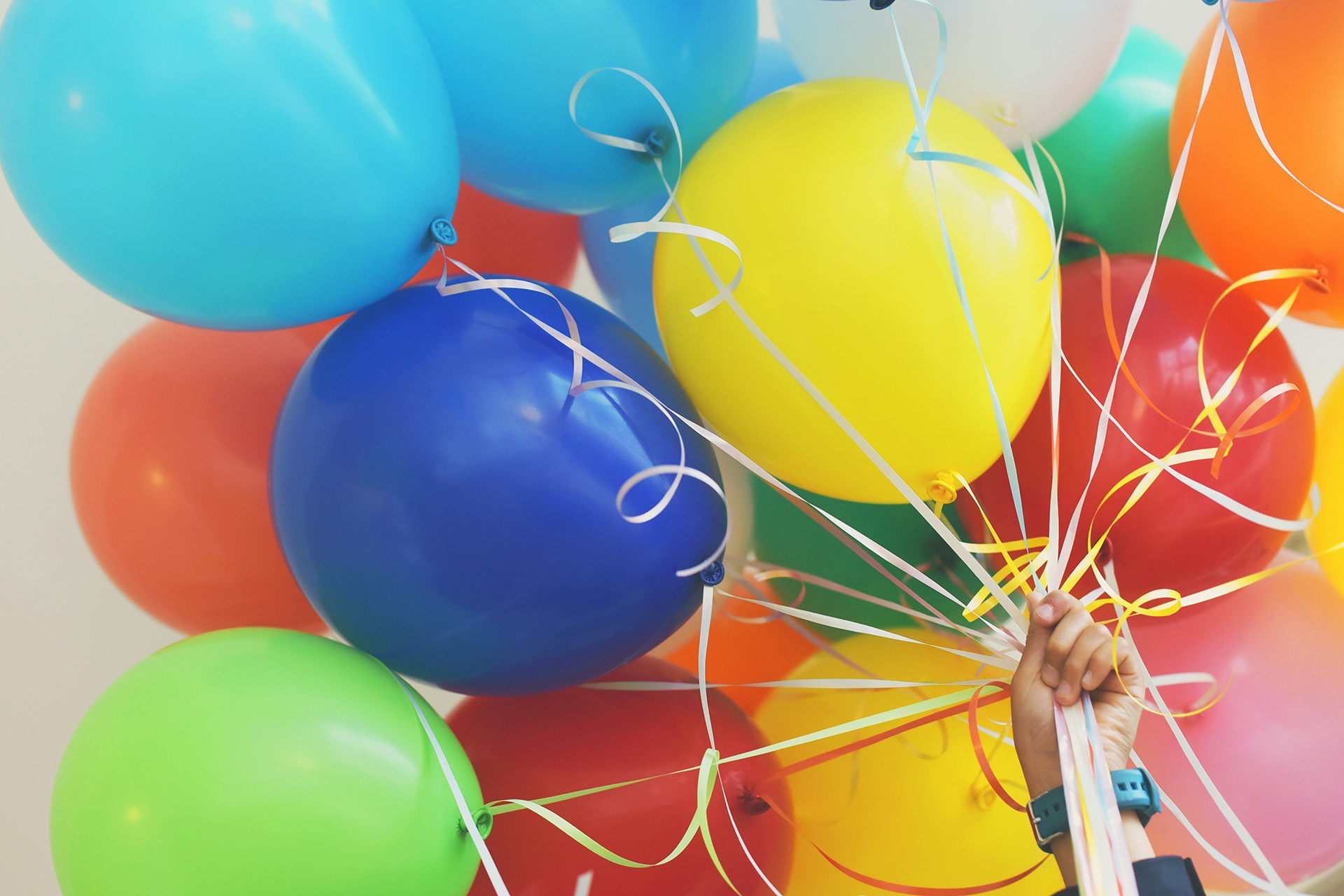 En hand håller i färgglada ballonger. 