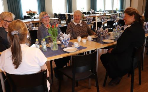 Personer sitter runt ett dukat bord, en stol är ledig.