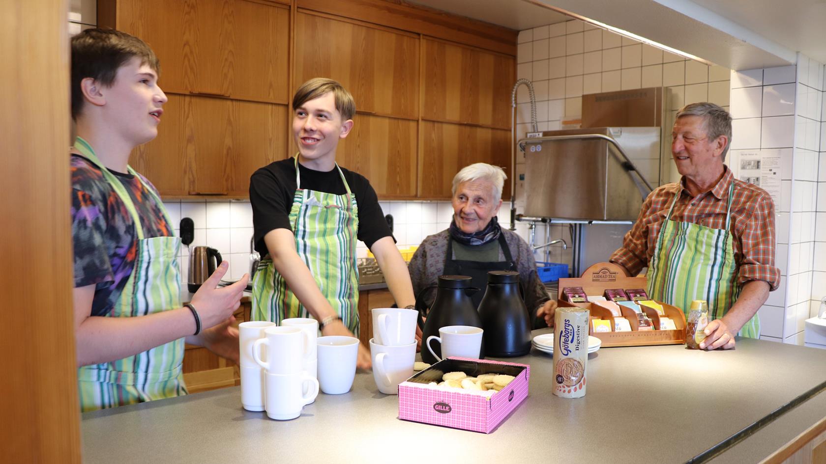 Fyra personer i olika åldrar står i köket och plockar fram koppar.