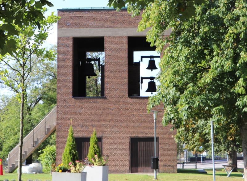 Ett fyrkantigt klocktorn i tegel där tre klockor kan ses genom de stora fönstren.