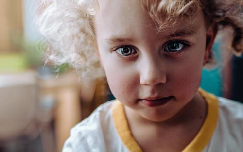 Ett barn med yvigt lockigt ljust hår tittar framåt.