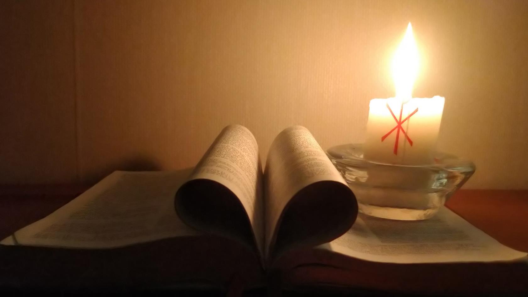 En uppslagen bibel där sidorna i mitten är vikta som ett hjärta. Rummet är upplyst av ett stearinljus.