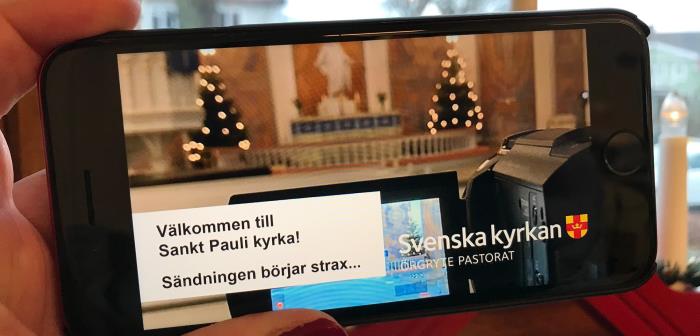 En hand håller en mobil där en gudstjänst ska börja livesändas.