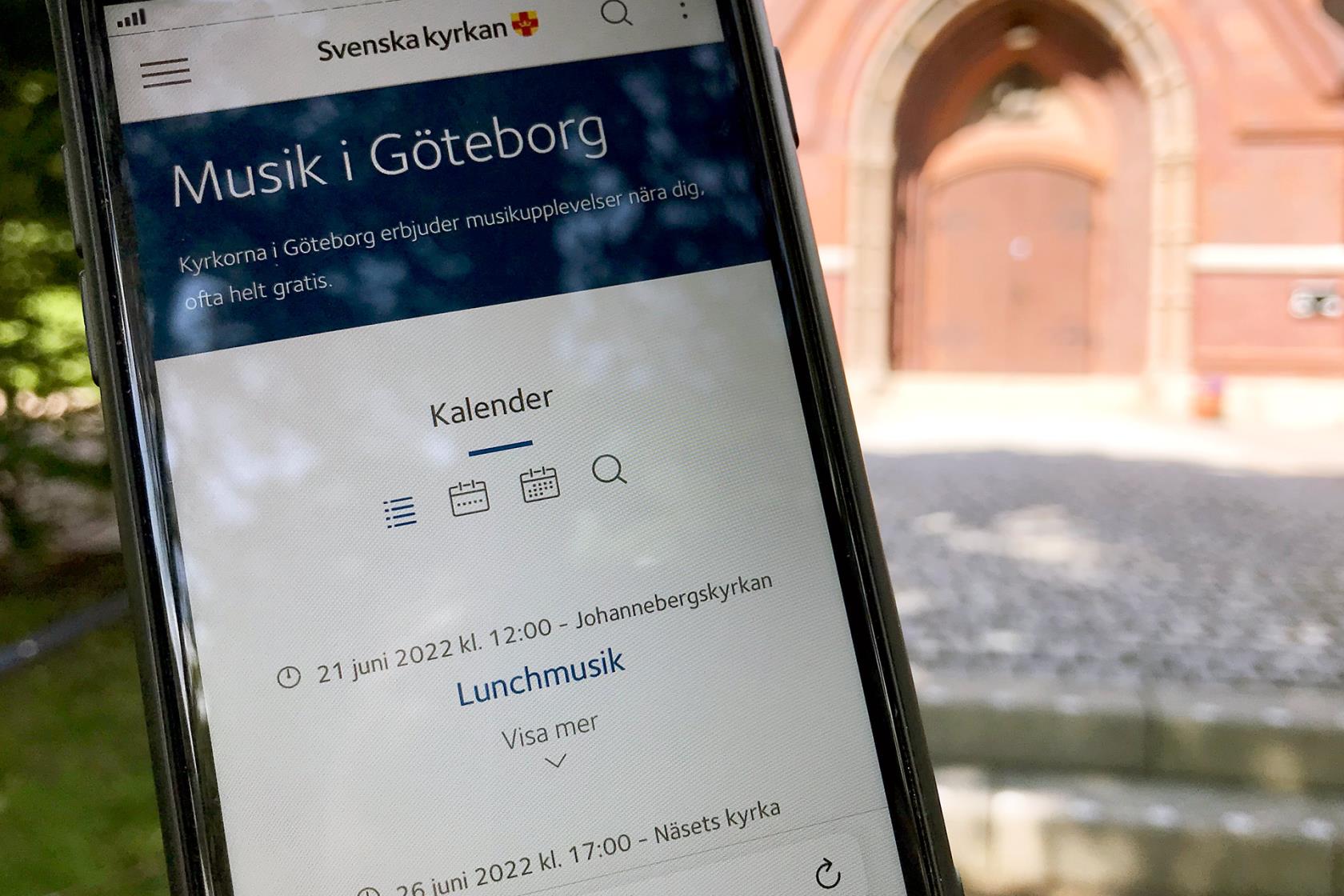 En mobiltelefon visar en kalender, i bakgrunden syns en kyrkport.