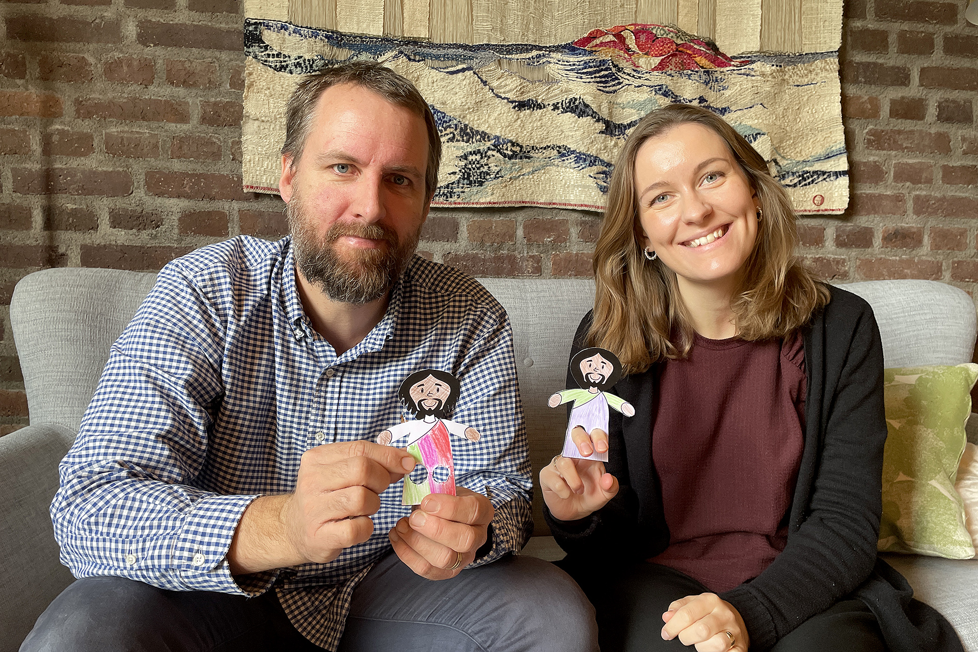 Två personer sitter i en soffa och håller upp två pappersfigurer.