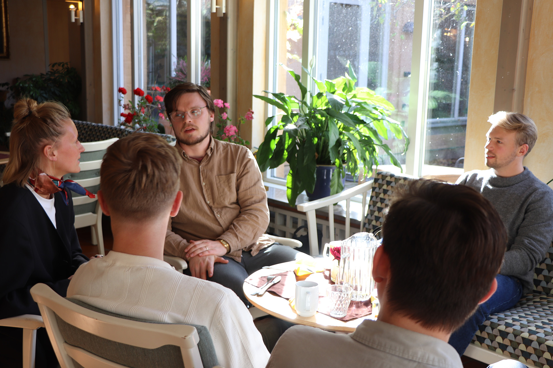 Fem personer sitter runt ett kaffebord och pratar. 