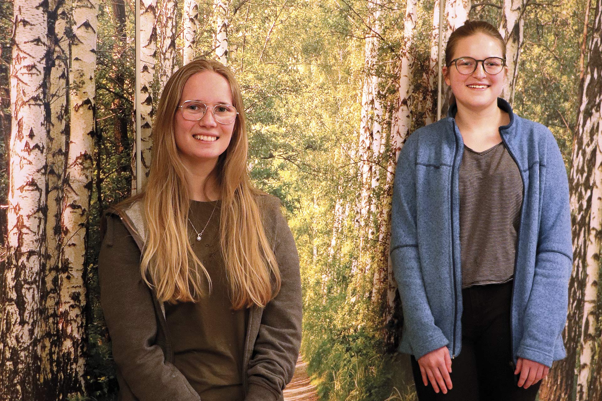 Två person står framför en vägg som föreställer en skog.