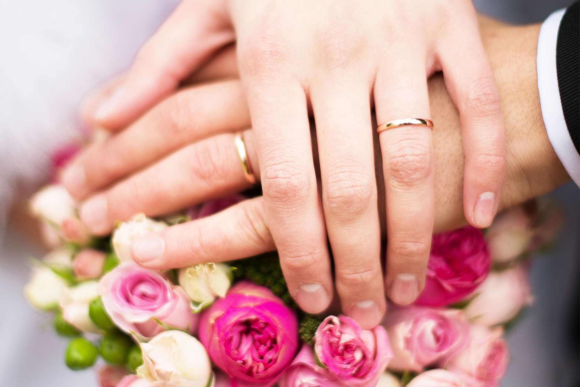 Händer med guldringar över en bukett med rosa rosor.