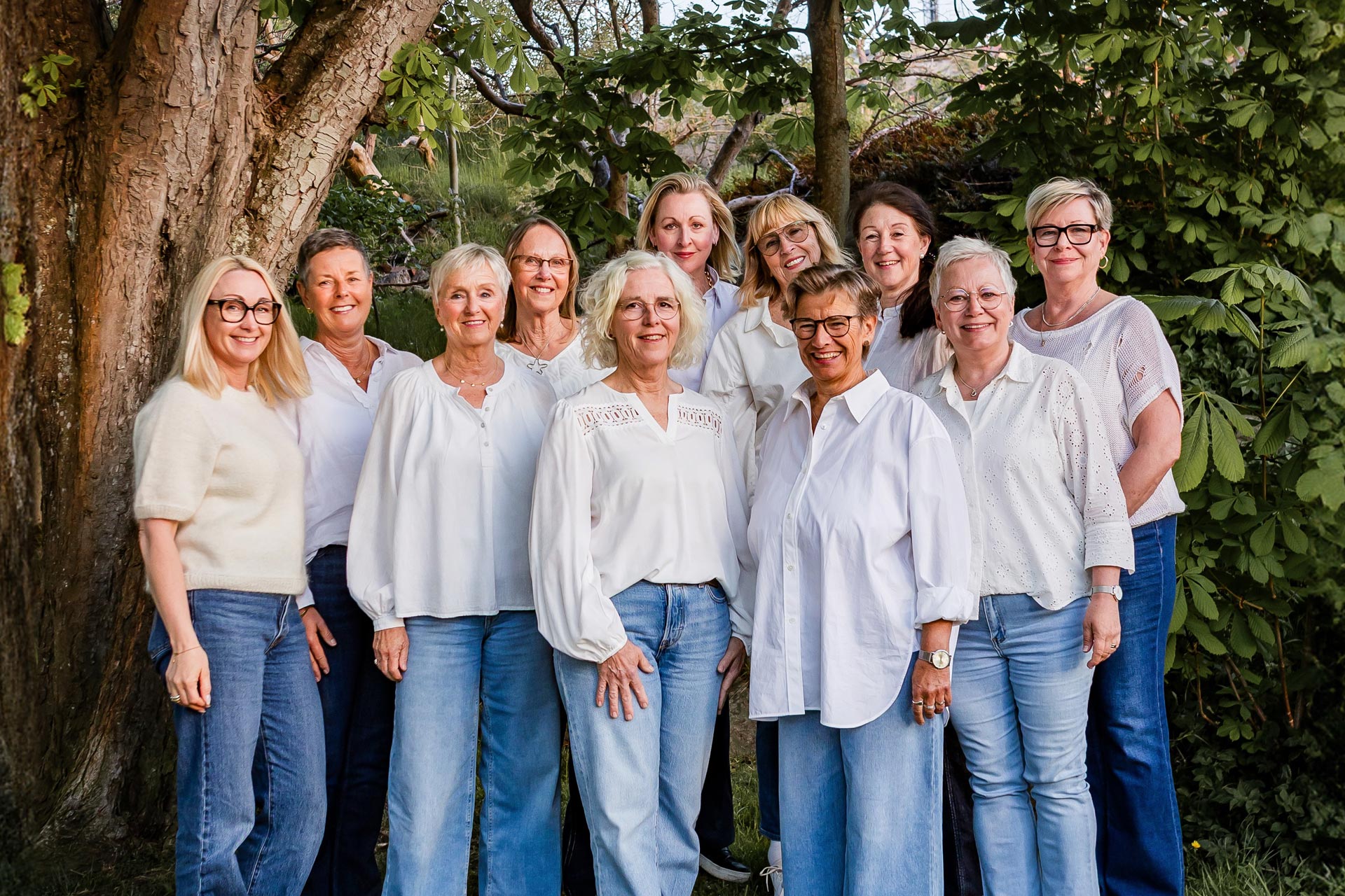 Körsångare står ute i grönskan, klädda i vitt och jeans.