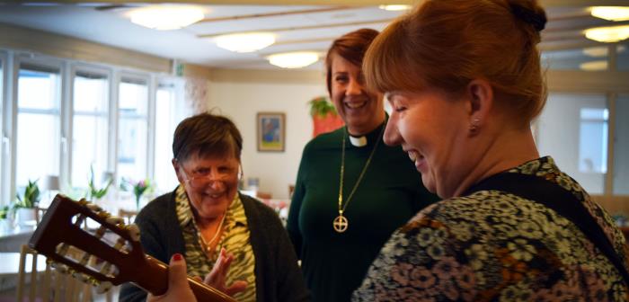 Person från kyrkan sjunger och spelar tillsammans med boende på serviceboende.