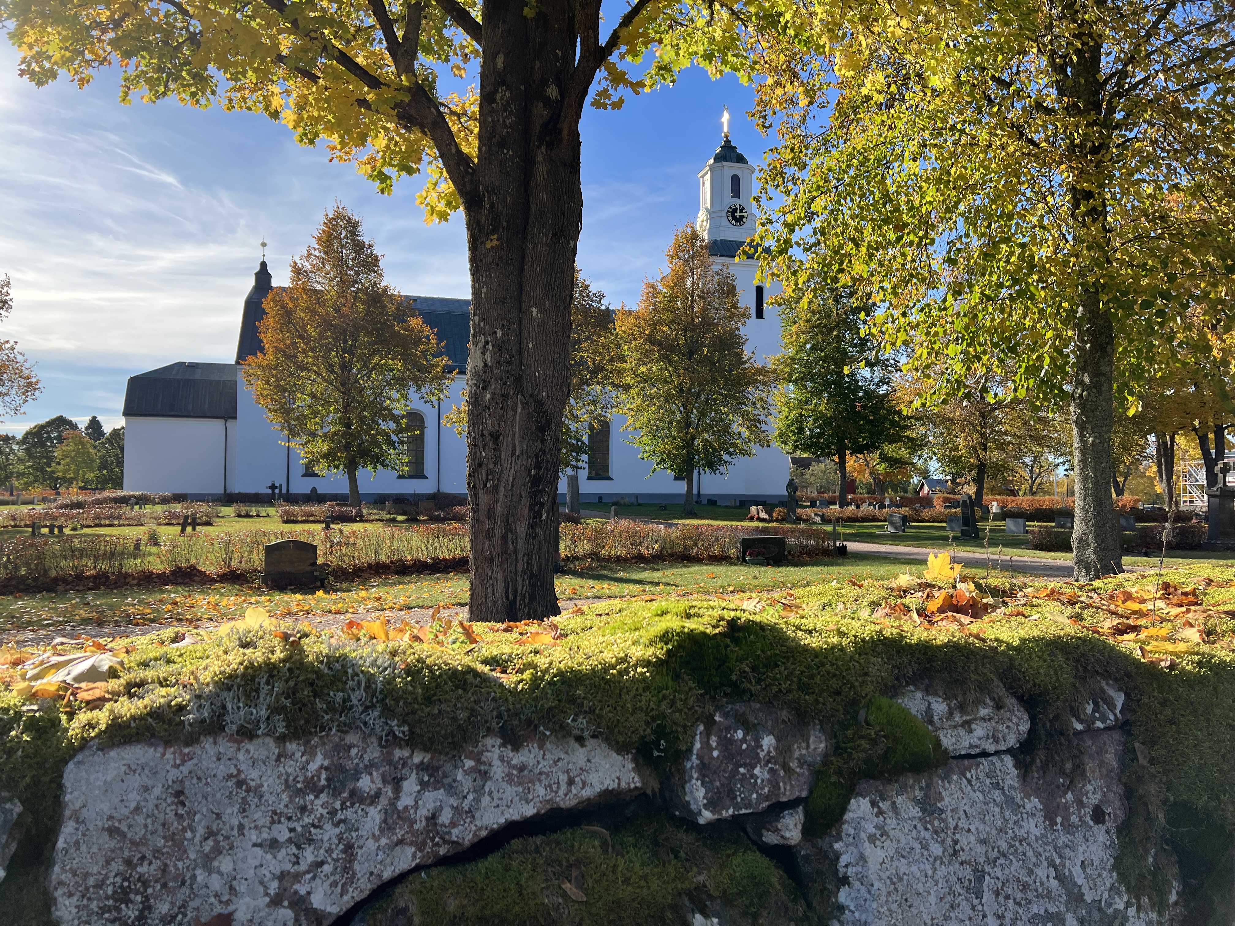 Hedesunda kyrka med stenmuren i förgrunden i höstsol