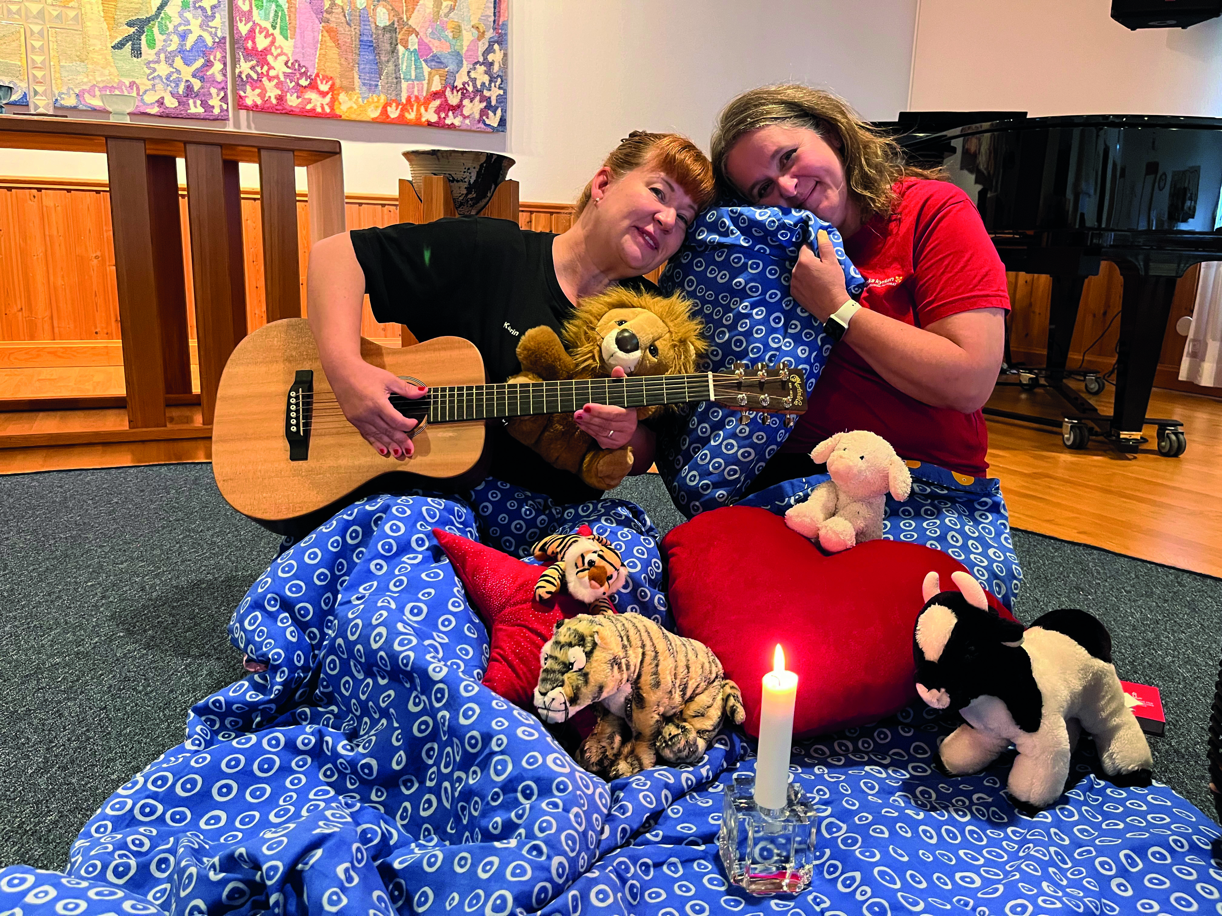 Två vuxna personer sitter på golvet och sjunger godnattsånger tillsammans med gosedjur.