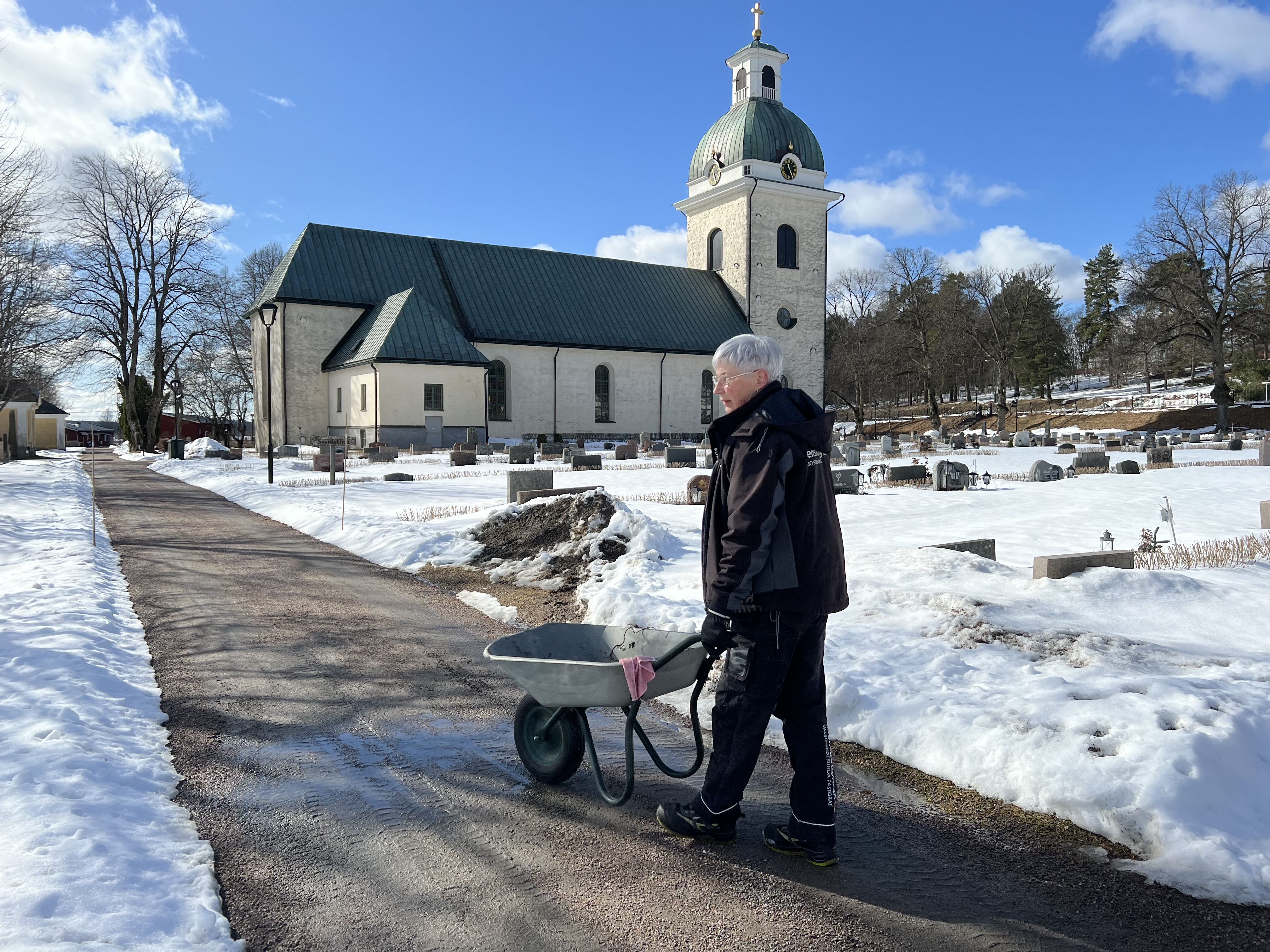 Kyrkogårdsarbetare med skottkärra på kyrkogården