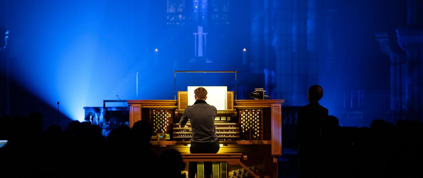 En organist spelar på en orgel i en kyrka, upplyst i blått.