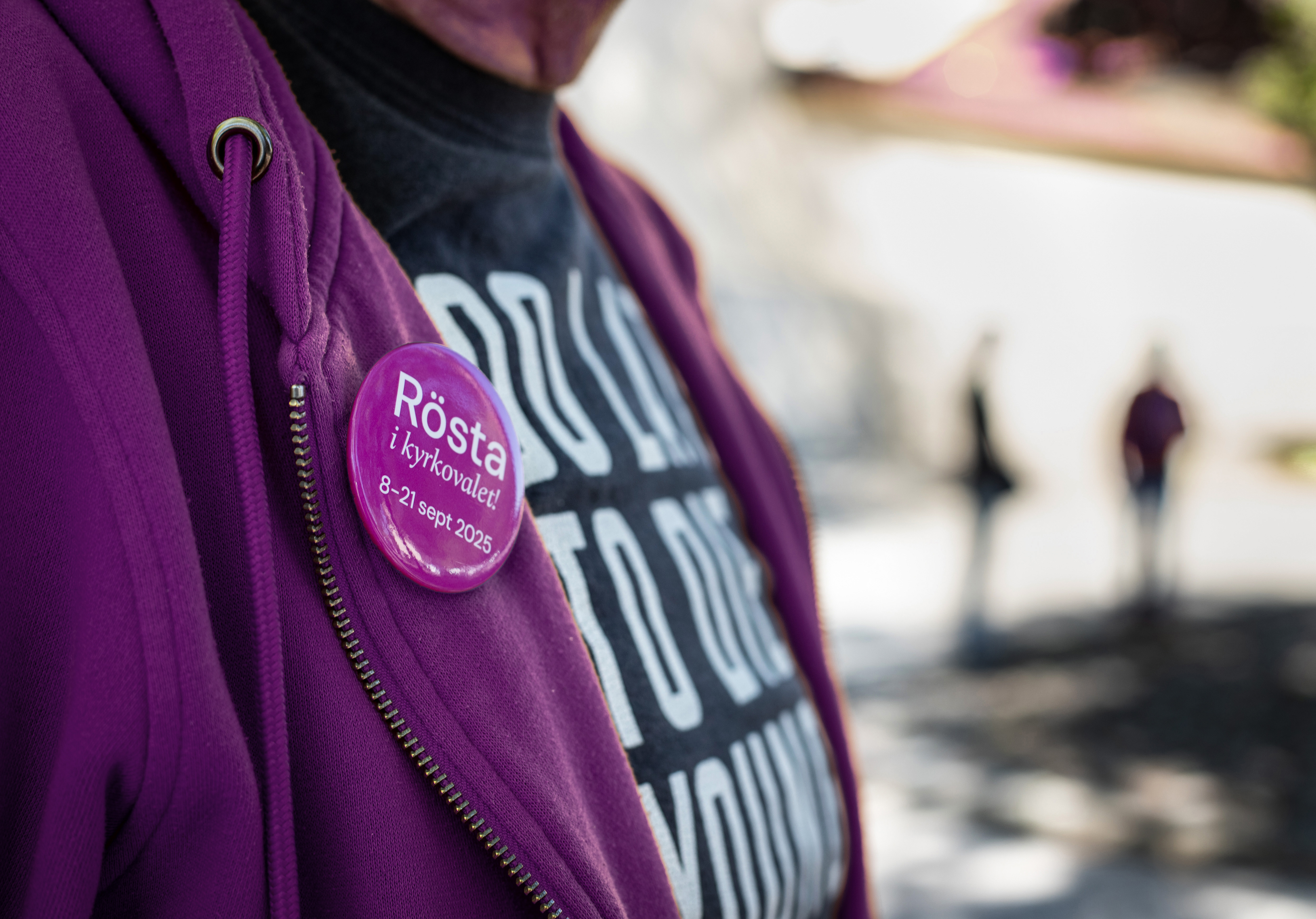 En närbild på en lila badge med texten "Rösta i kyrkovalet 8-21 september 2025". Badgen är fäst på en persons zip-tröja.
