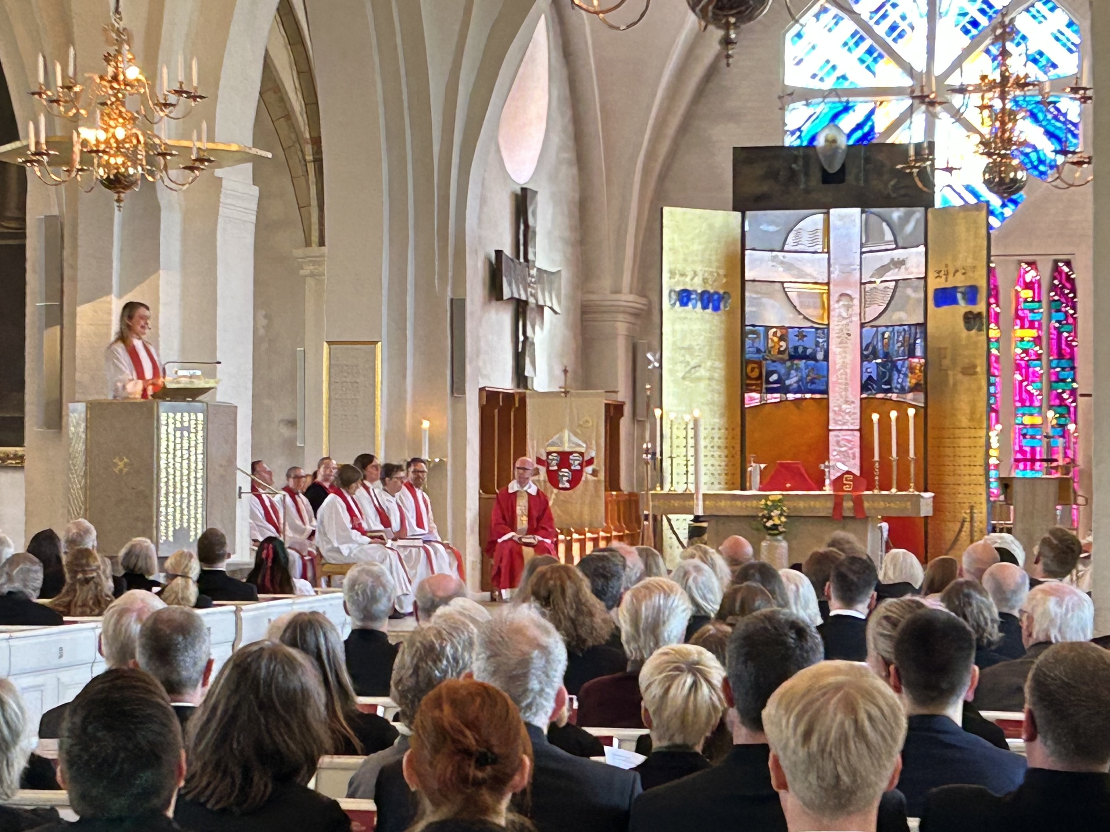 Inledningsmässan i Växjö domkyrka. I koret syns präster och diakoner i liturgiska kläder med röd färg. Prästen Maria Jukes står i predikstolen. Bänkraderna är fyllda.