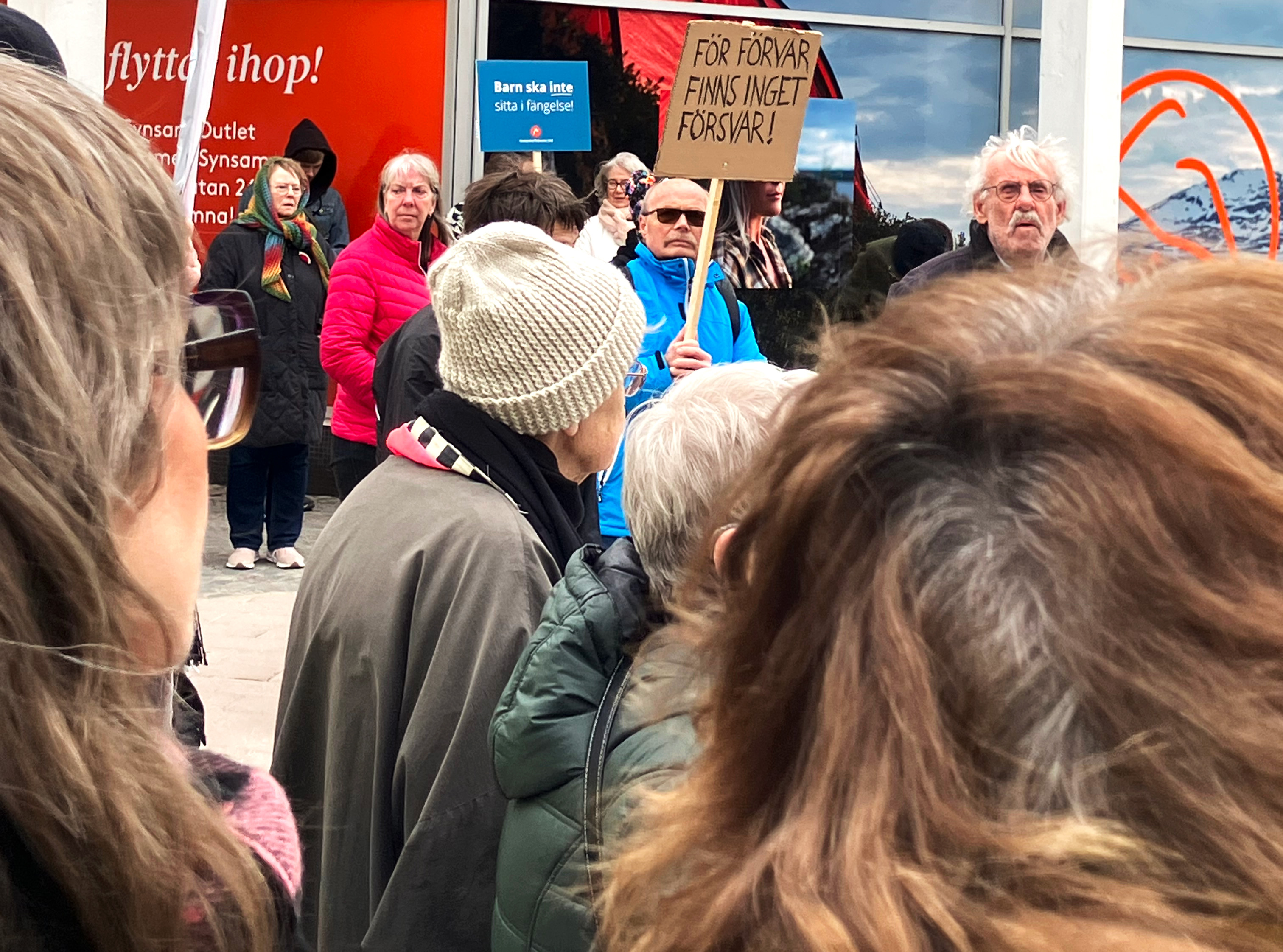 Folksamling vid manifestationen i Växjö. Två personer bär skyltar med budskapen "Barn ska inte sitta i fängelse" och "För förvar finns inget försvar".