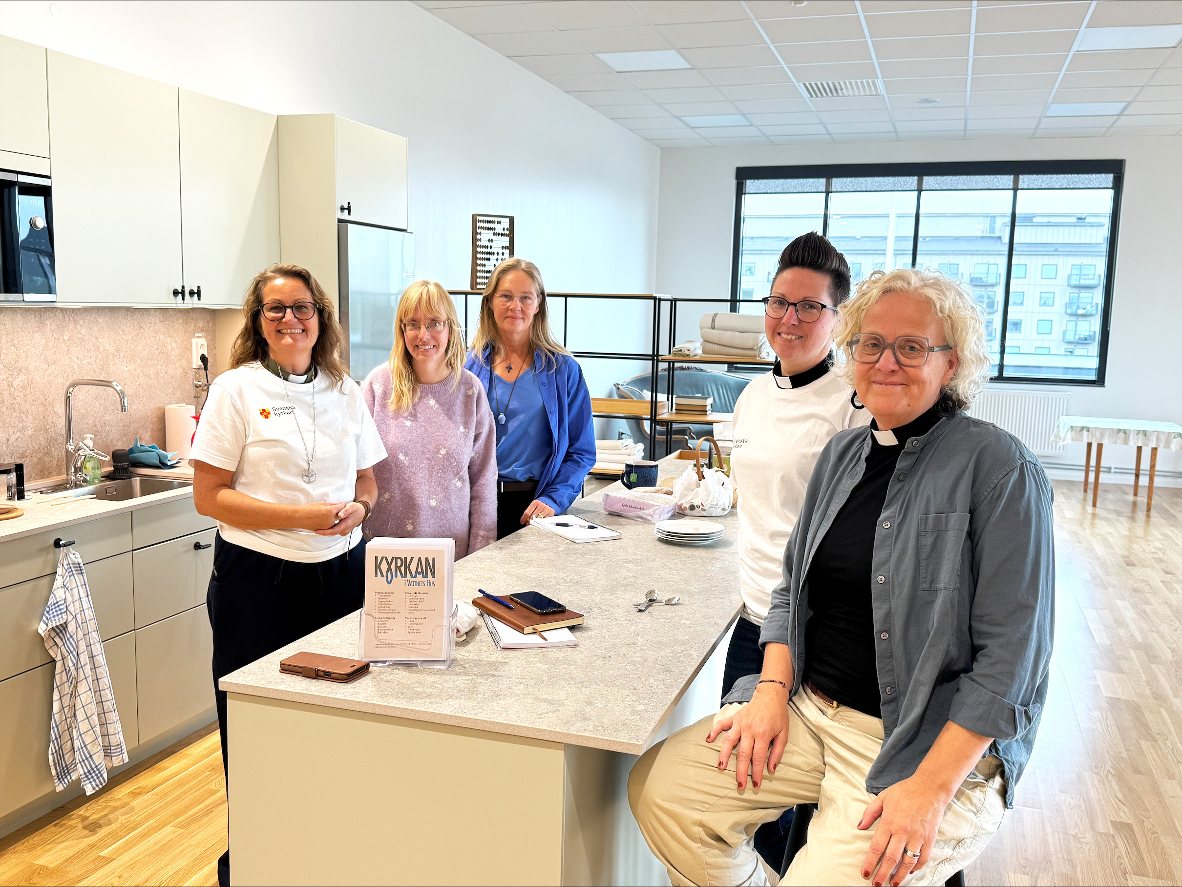 Fem kvinnor står runt en köksö i en stor och ljus lokal. I bakgrunden syns köket och ett stort fönster.