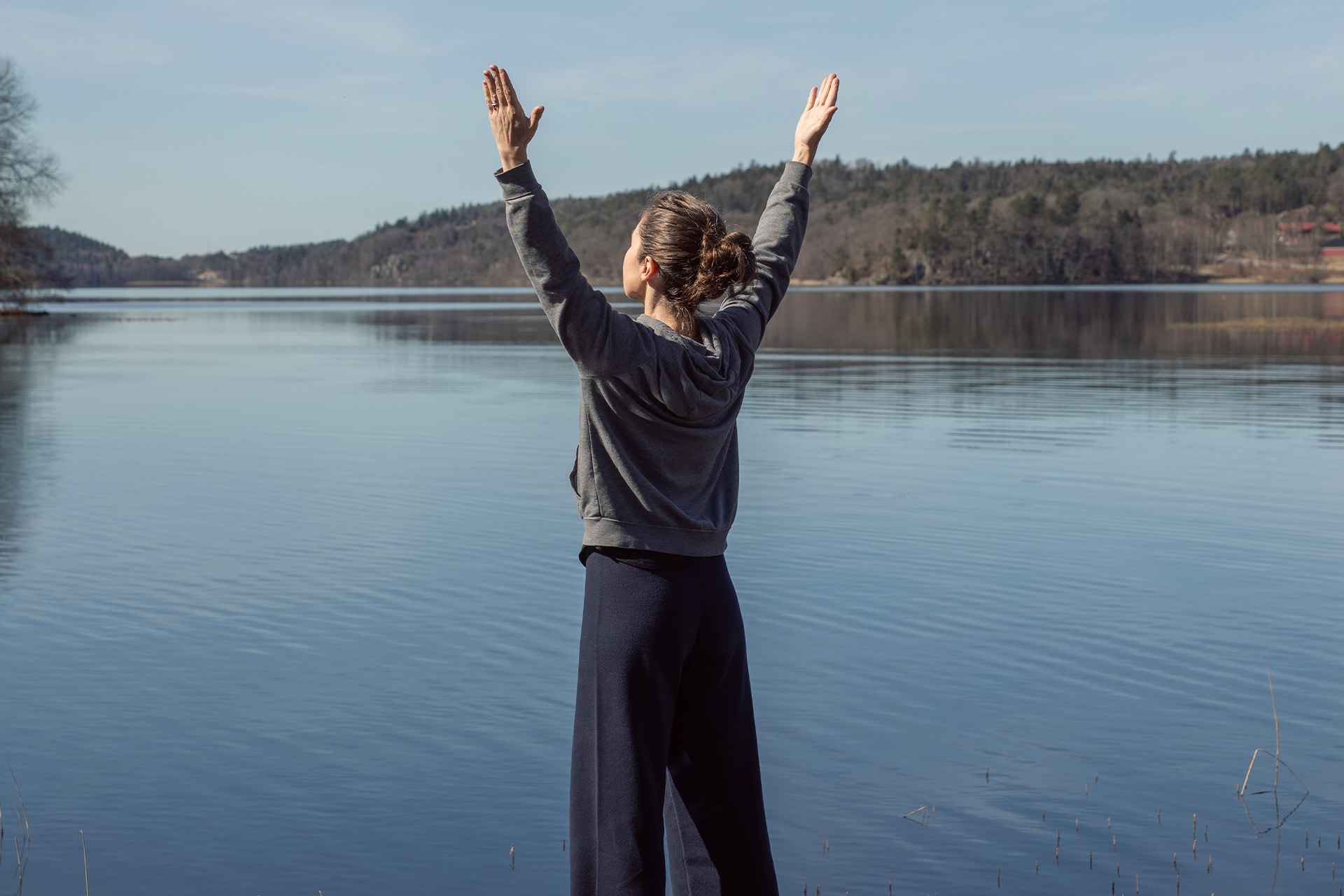 Kvinna som sträcker händerna mot himlen framför en spegelbland sjö. 