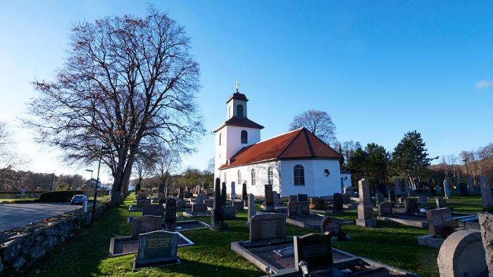 En vitkalkad kyrka med gravar på en kyrkogård framför kyrkan. Blå himmel och det är höst.