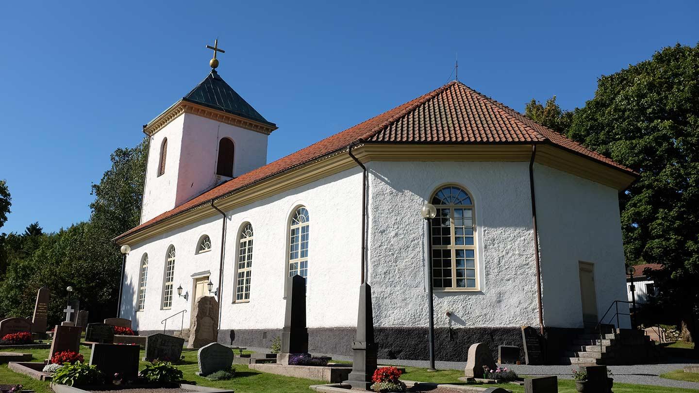 Härryda kyrka - en vitkalkad kyrka byggd 1850 omgiven av en kyrkogård med grön gräsmatta, utanför vilken finns stora gröna lövträd