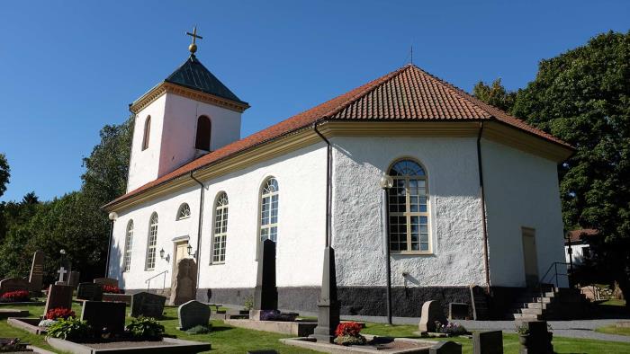 Härryda kyrka - en vitkalkad kyrka byggd 1850 omgiven av en kyrkogård med grön gräsmatta, utanför vilken finns stora gröna lövträd