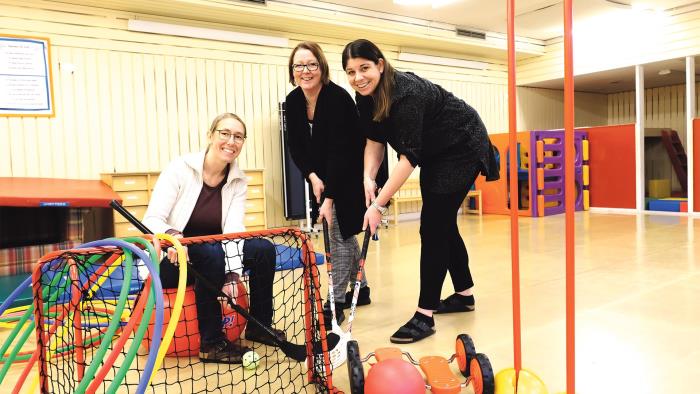 Tre pedagoger på Duvan i en leksal inomhus. Ett innebandymål i förgrunden. Alla håller en innebandyklubba i handen.