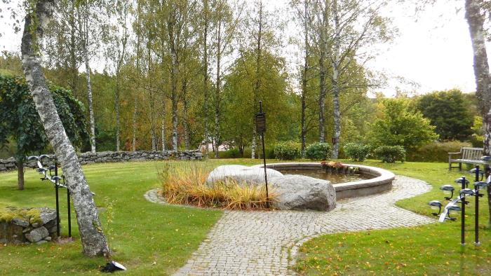 Minneslunden på Härryda kyrkogård. En stenomgärdad granitfontän med två stora stenblock framför. I förgrunden en björk.